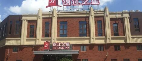 A hotel with a red and beige facade, a prominent sign, and a parking area in front.