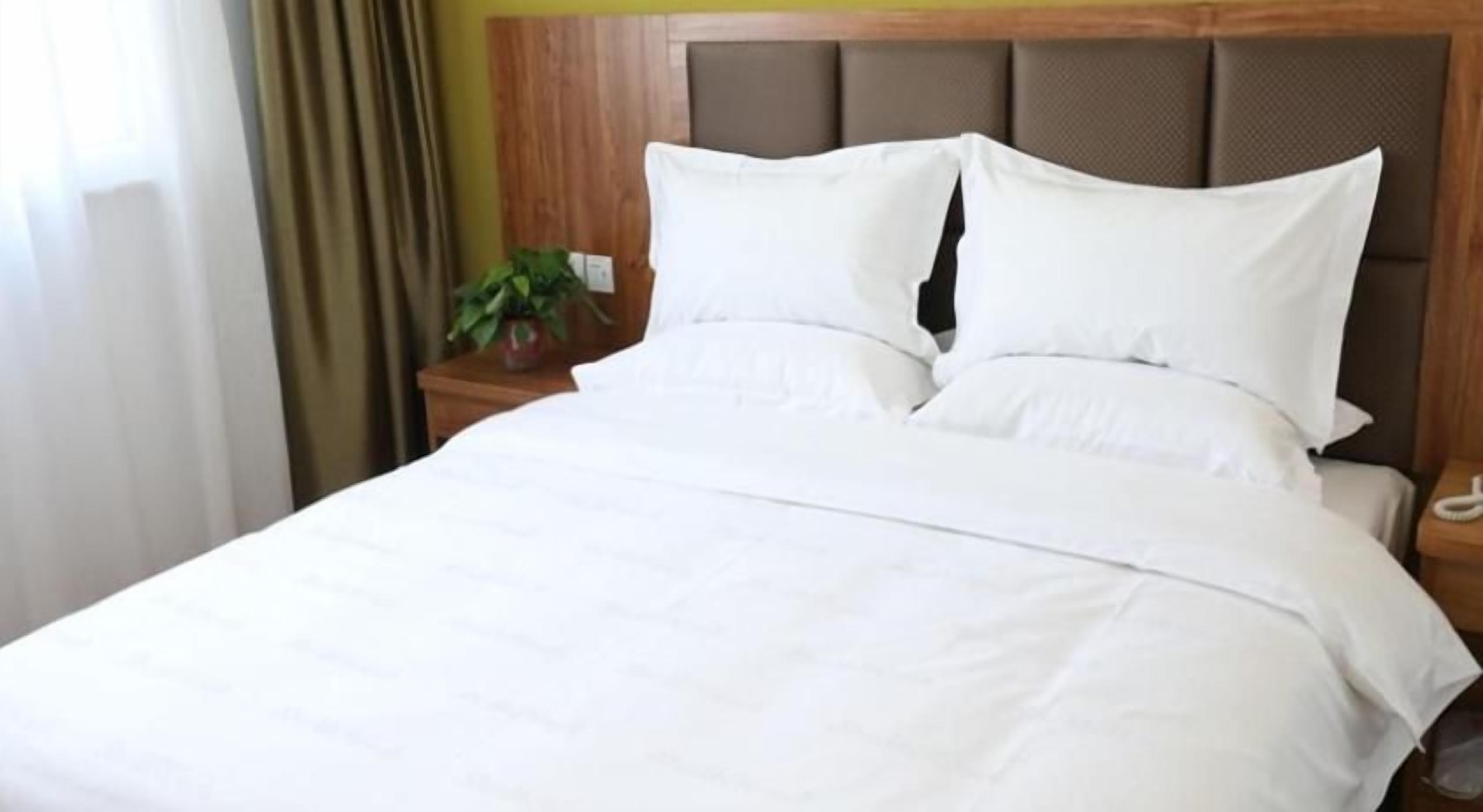 A neatly made bed with white linens and a wooden headboard.
