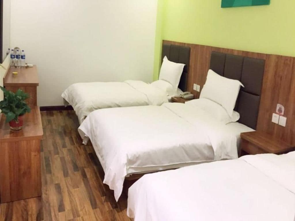A hotel room with three beds, a wooden nightstand, a telephone, and a green wall.