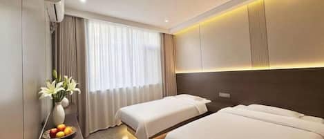 A hotel room with two beds, a bedside table with a vase of flowers, and a large window with curtains.