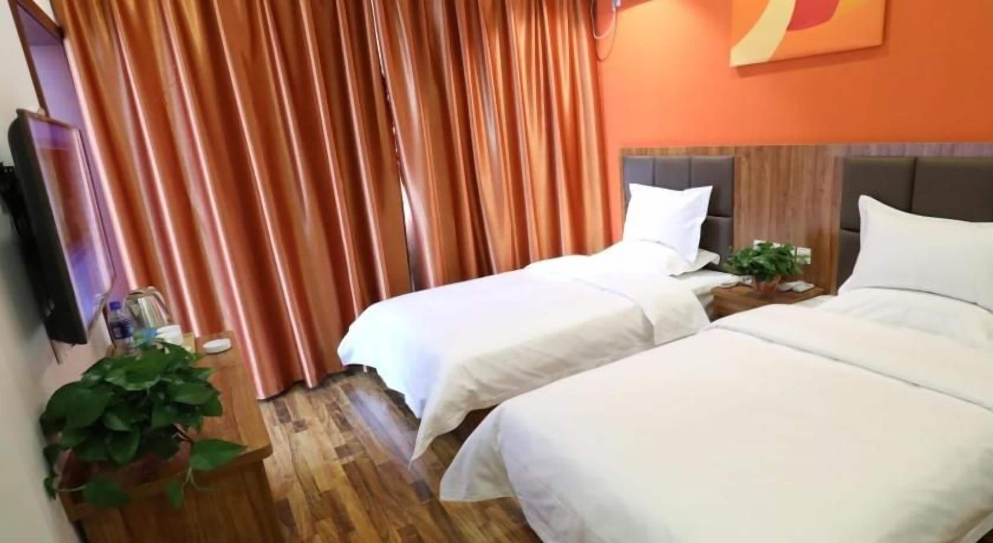 A hotel room with two beds, a wooden floor, a TV, and a plant.