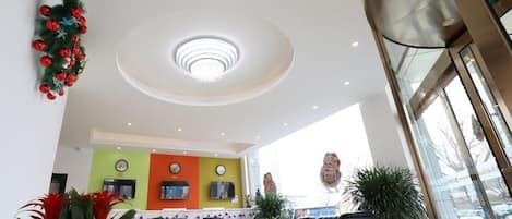 A hotel lobby with a reception desk, seating area, and a decorative ceiling light.