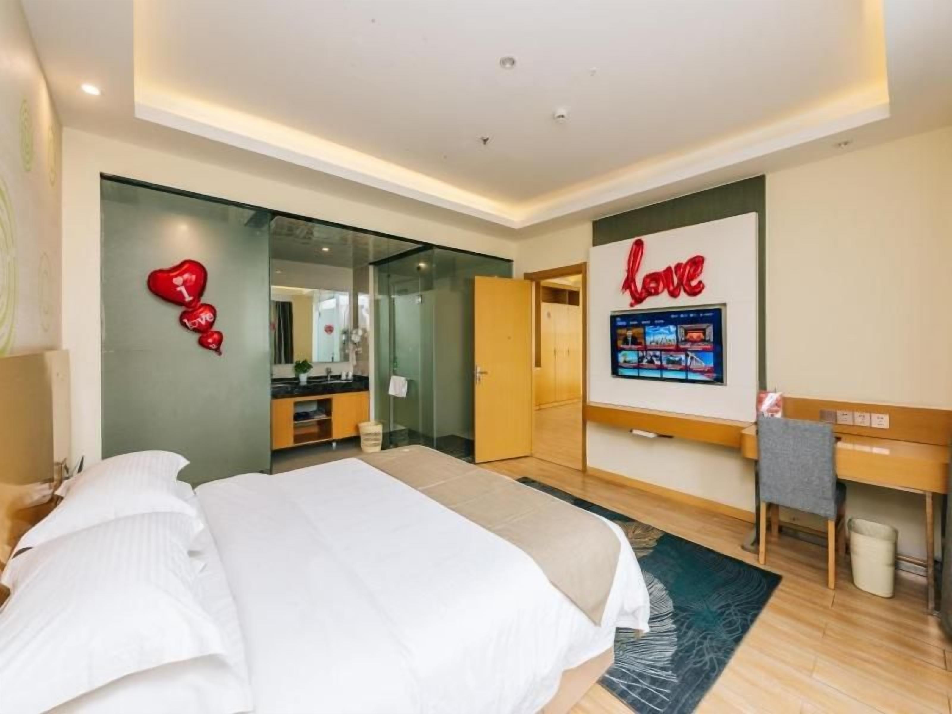 A hotel room with a bed, a desk, a TV, and a wall with a heart-shaped decoration.