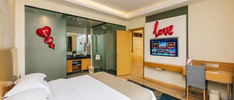 A hotel room with a bed, a desk, a TV, and a wall with a heart-shaped decoration.