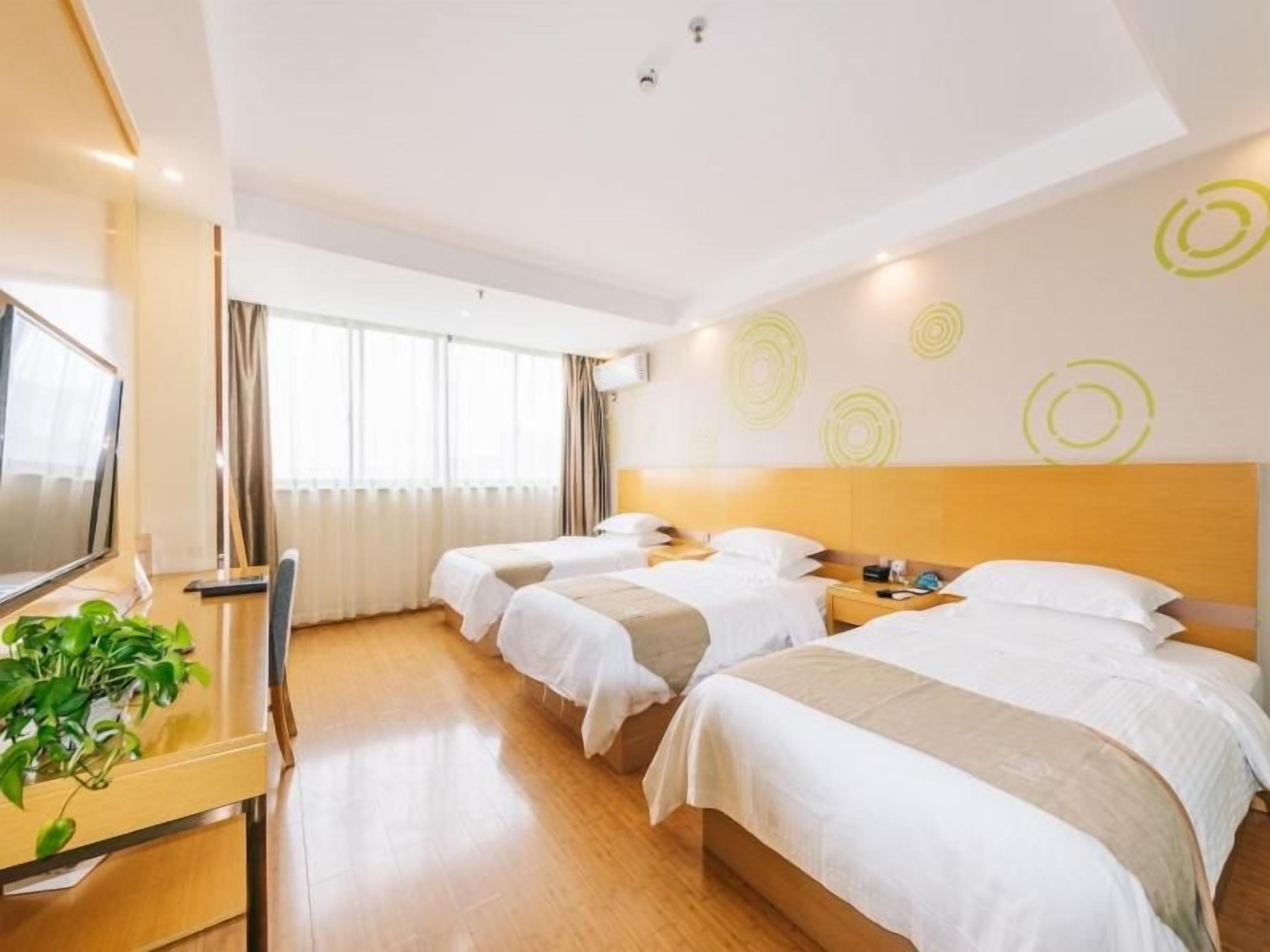 Habitación de hotel con dos camas, un escritorio con televisor y una ventana con cortinas.