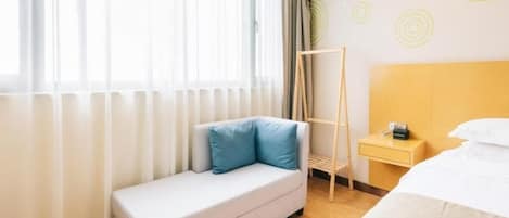 Habitación de hotel con cama, sofá, mesita de noche y ventana con cortinas.