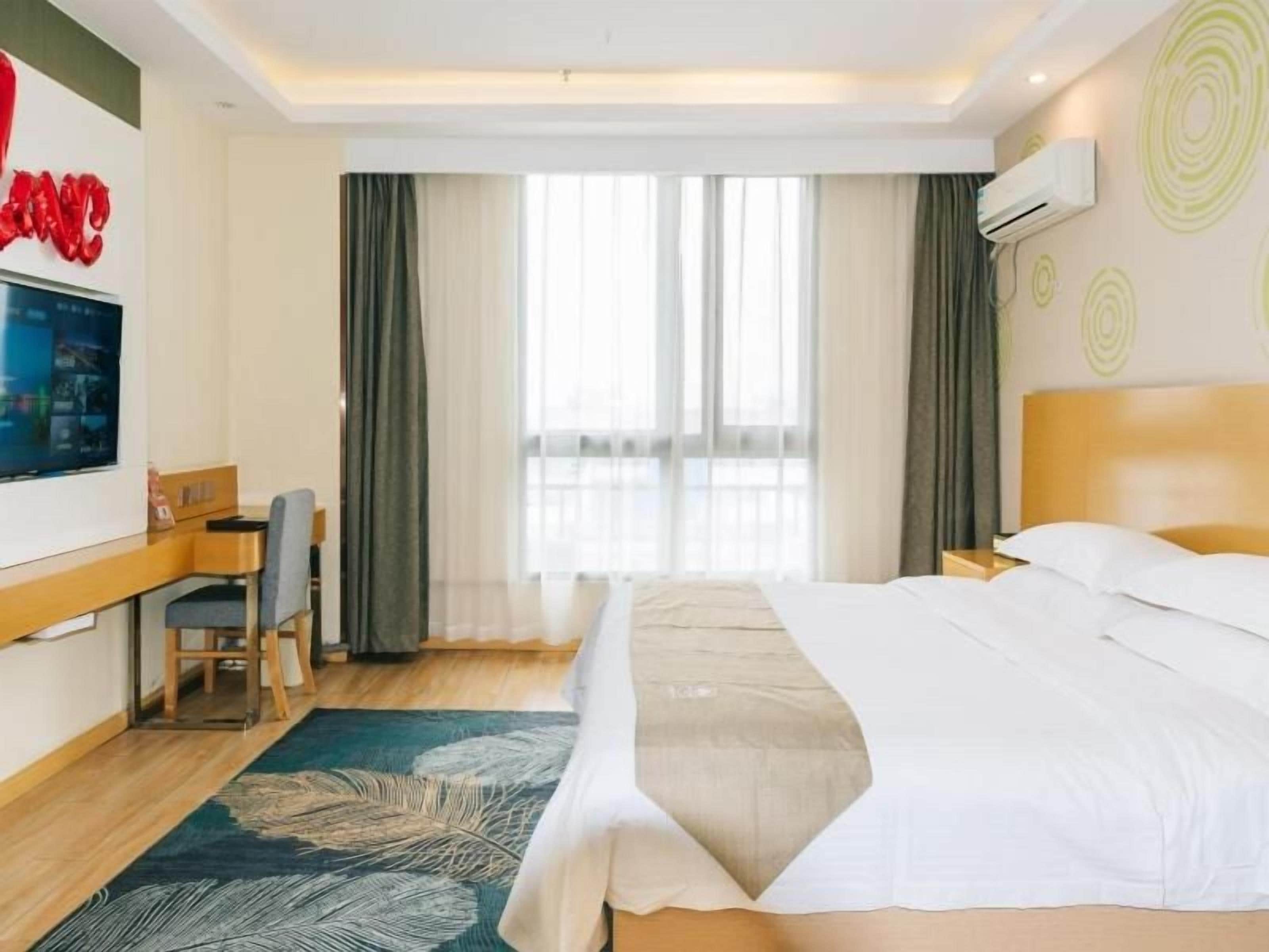 Una habitación de hotel con cama, escritorio, silla, televisor y ventana con cortinas.