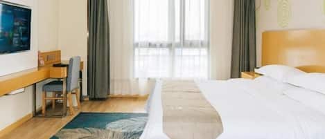 Una habitación de hotel con cama, escritorio, silla, televisor y ventana con cortinas.