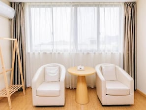 A room with two white armchairs, a round wooden table, and a window with sheer curtains. - Greentree Inn Jiangyin Bus Station Meiyuan Street Express Hotel (Wuxi)