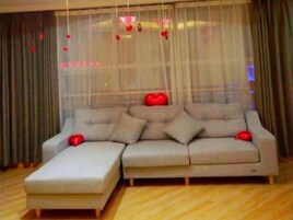 Uma sala de estar moderna com sofá seccional, mesa de centro e uma janela grande com cortinas leves e decorações em formato de coração.