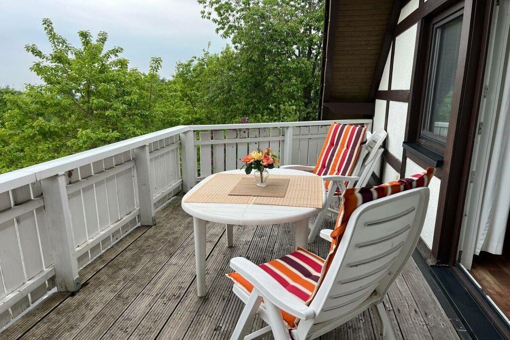 Un balcon avec une table et des chaises blanches, une petite plante en pot et une vue sur la verdure.