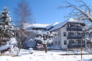 Ein mehrstöckiges Gebäude mit Balkonen, umgeben von schneebedeckten Bäumen und einem klaren Himmel.