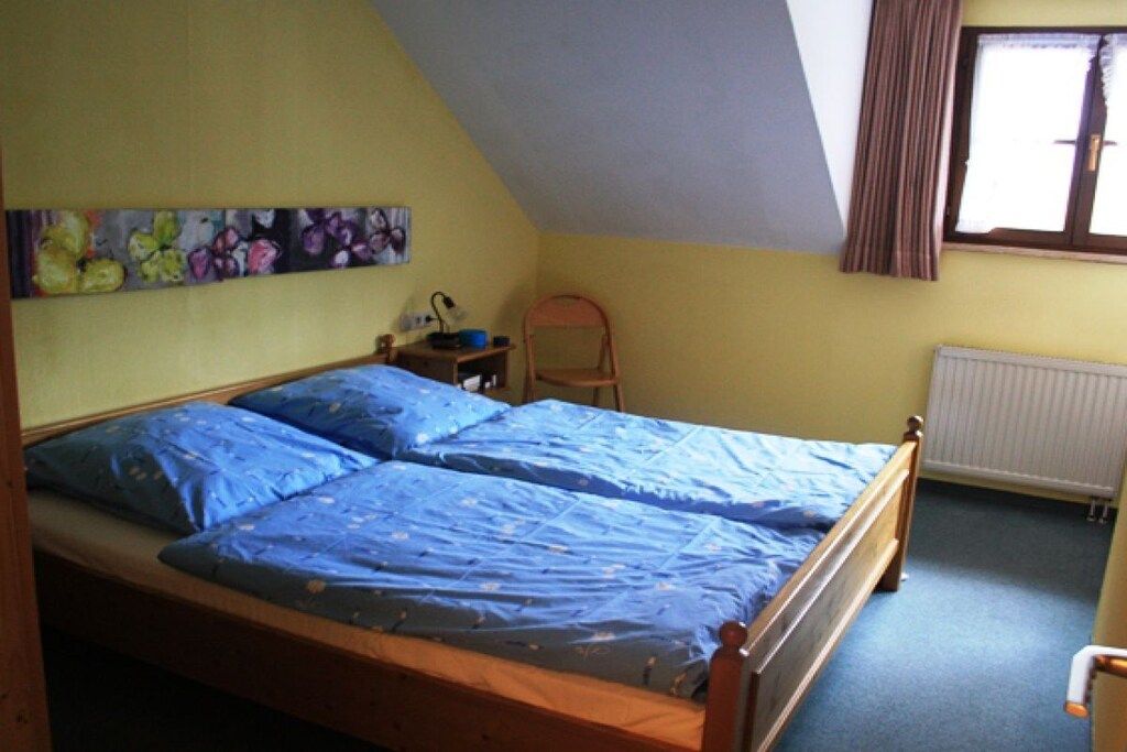 Ein Schlafzimmer mit einem Einzelbett, einem Heizkörper, einem Fenster mit Vorhängen und einem Bild an der Wand.