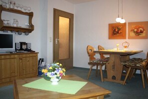 Un coin repas comprenant une table en bois, des chaises, un vase de fleurs, un téléviseur et un buffet en bois.