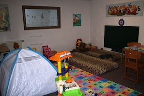 Une salle de jeux pour enfants avec une tente, des jouets, un tapis de jeu avec des lettres, une télévision et une cible accrochée au mur.