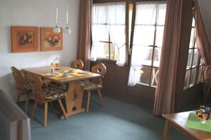 Ein Essbereich mit einem Holztisch und Stühlen, einem kleinen Beistelltisch mit einer Vase sowie zwei gerahmten Bildern an der Wand.