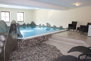 Ein Hallenbad mit Steinrand, einer Rutsche und einem Sitzbereich mit Stühlen.