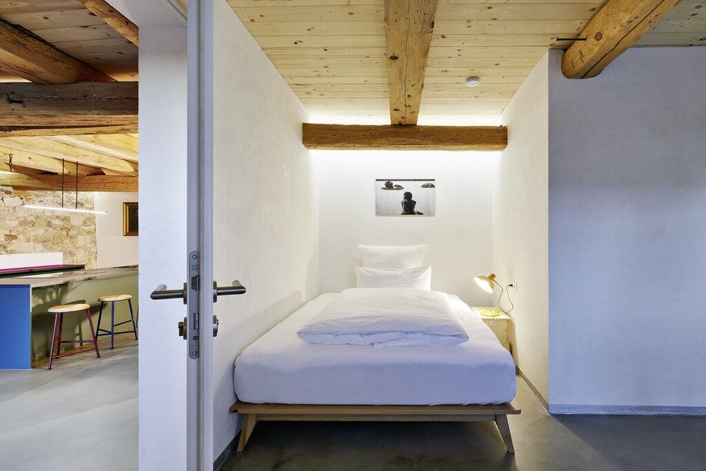 A bedroom with a bed, a nightstand, a wall-mounted picture, and a door leading to a bathroom.