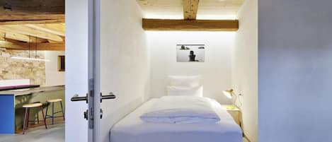 A bedroom with a bed, a nightstand, a wall-mounted picture, and a door leading to a bathroom.