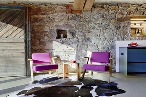 A room with a stone wall, two purple chairs, a small wooden table, and a cowhide rug. - Holiday apartment with 2 bedrooms (Löffingen)