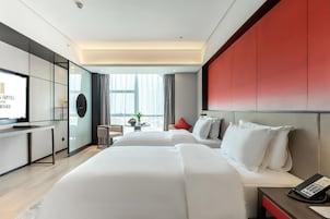 Habitación de hotel con dos camas, un escritorio, televisor, teléfono y vista a la ciudad.