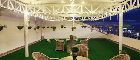 An indoor patio area with wicker furniture and hanging plants, featuring a white ceiling structure and artificial green turf.
