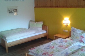 Habitació petita amb dos llits individuals, una tauleta de nit, una làmpada fixada a la paret i un quadre al mur.
