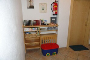 A small room with a wooden shelf containing books and cans, a red and blue toy, a fire extinguisher, and a door. - Holiday apartment with 2 bedrooms (Rauris)