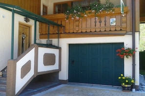 A two-story building with a green door, a balcony with flowers, and a small garden area. - Holiday apartment with 2 bedrooms (Rauris)