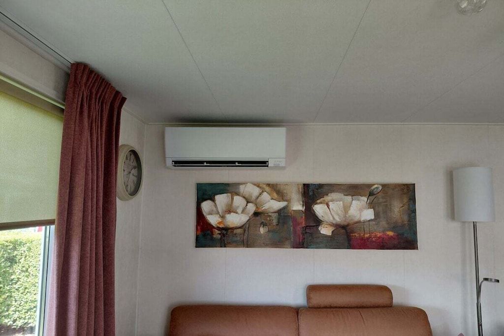 Una habitación con un sofá marrón, un reloj, un equipo de aire acondicionado y un cuadro de flores en la pared.