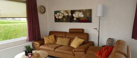 A living room with a brown sofa, a round coffee table, a floor lamp, and a painting of flowers on the wall.