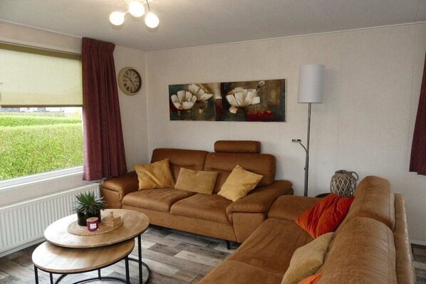 A living room with a brown sofa, a round coffee table, a floor lamp, and a painting of flowers on the wall. - Cottage in Serooskerke with swimming pool (Serooskerke)