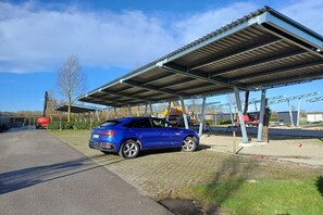 A parking area with a covered shelter, a blue car parked, and a clear sky.