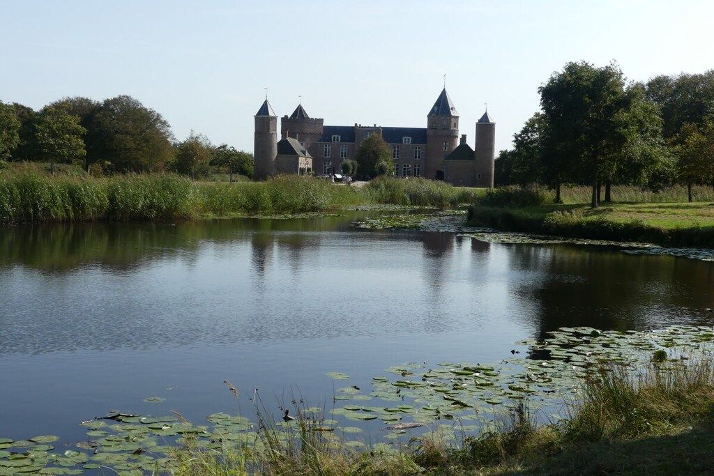 A historic building with multiple towers, a moat, and a pond with lily pads.