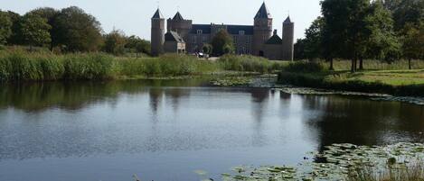Ein historisches Gebäude mit mehreren Türmen, einem Burggraben und einem Teich mit Seerosen.