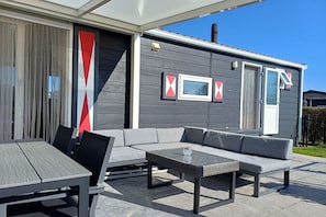 An outdoor patio area with a dining table, chairs, a sofa, and a small table. - Cottage in Serooskerke with swimming pool (Serooskerke)