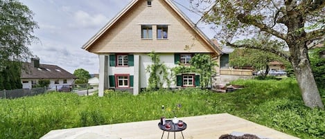 A two-story house with a sloped roof, a balcony, and a garden area.
