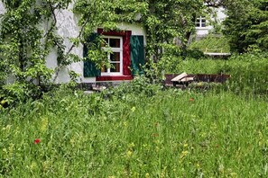A rustic house with a red door and green shutters, surrounded by a lush garden. - Holiday apartment with 2 bedrooms (Löffingen)