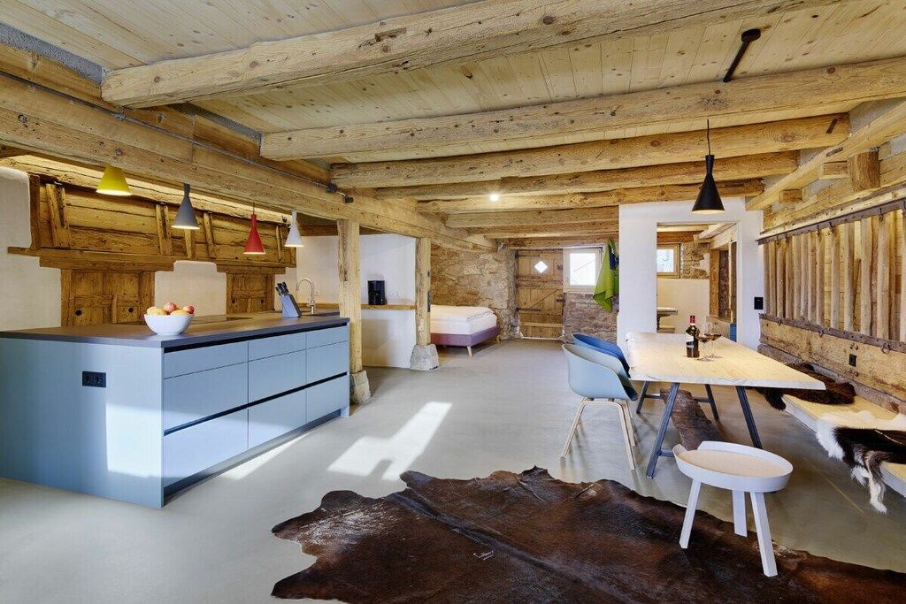 A rustic interior with a kitchen, dining area, and a stone wall.