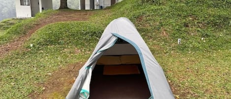 A tent set up on a grassy slope with a building in the background.