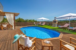 Eine Holzterrasse mit Swimmingpool, Liegestühlen und Sonnenschirmen.