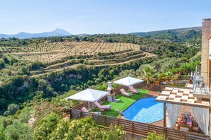 Ein Poolbereich mit Liegestühlen und Sonnenschirmen, umgeben von üppiger Vegetation und terrassenförmigen Feldern.