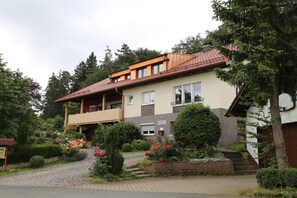 Ein zweistöckiges Wohngebäude mit Balkon, einem Blumengarten und einem gepflasterten Zufahrtsweg.