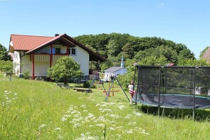 Ein Haus mit rotem Dach, einem Trampolin und einer Schaukel auf einer Rasenfläche.