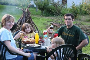 A family dining outdoors with a table set for a meal, surrounded by greenery. - 2 Houses on the edge of the forest (Leutenbach)