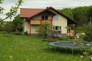 Ein Haus mit rotem Dach, einem Balkon und einem Trampolin im grünen Garten.