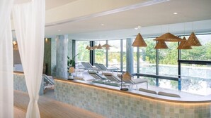 Uma área de spa com balcão de recepção, espreguiçadeiras e amplas janelas com vista para o exterior.