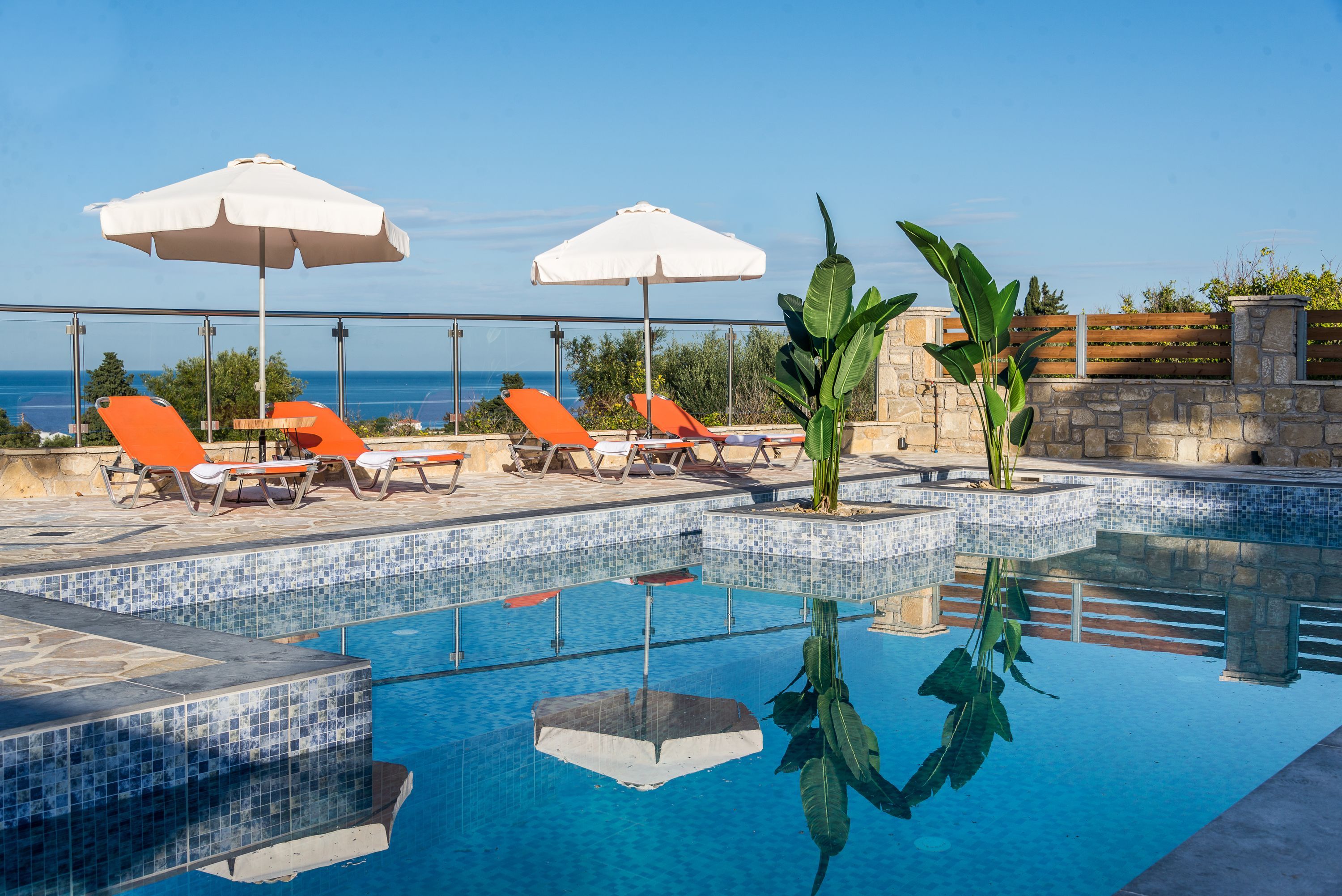 Ein Poolbereich mit Fliesenböden, Liegestühlen und Sonnenschirmen.