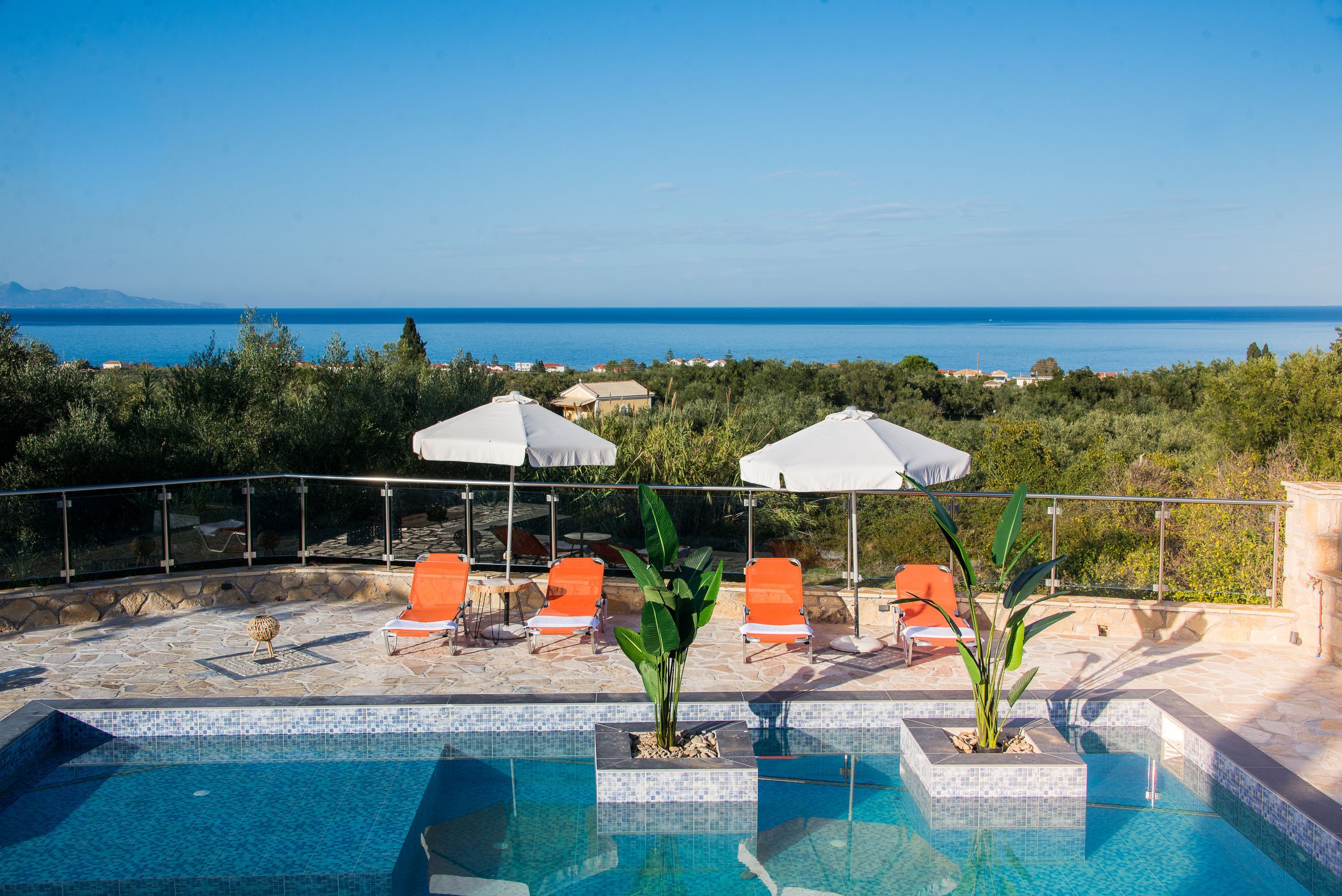 Zona de piscina con vista despejada al mar y un paisaje montañoso al fondo.