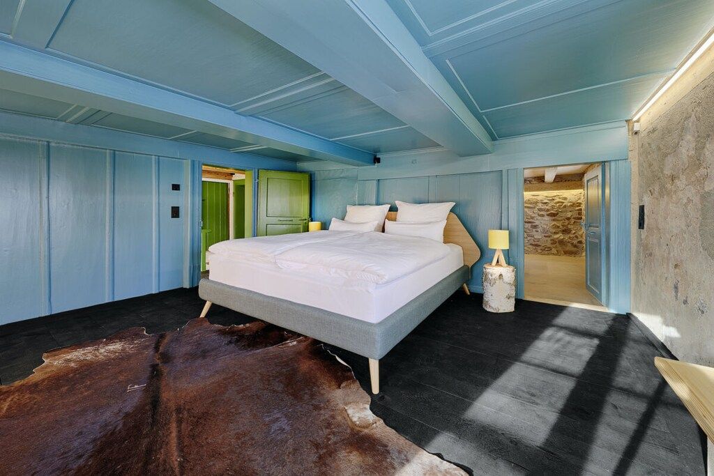 A bedroom with a large bed, a wooden floor, a cowhide rug, and a stone wall.